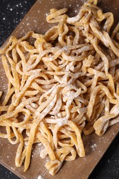 Board with homemade pasta and flour on dark table, top view