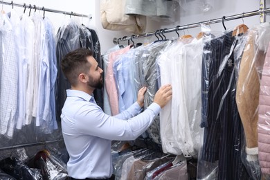 Photo of Dry-cleaning service. Worker choosing clothes from rack indoors