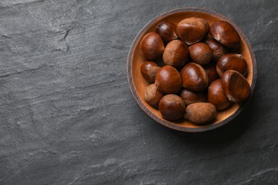 Roasted edible sweet chestnuts in bowl on grey textured table, top view. Space for text