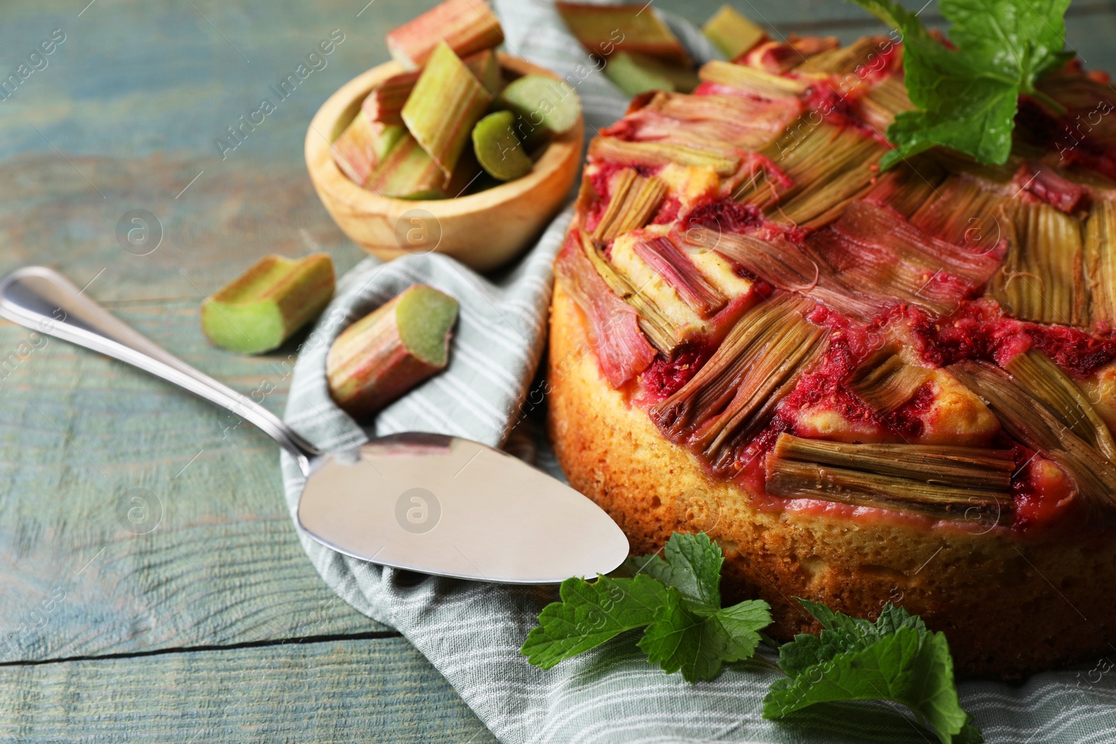 Photo of Freshly baked rhubarb pie, green leaves and cake server on wooden table, closeup. Space for text