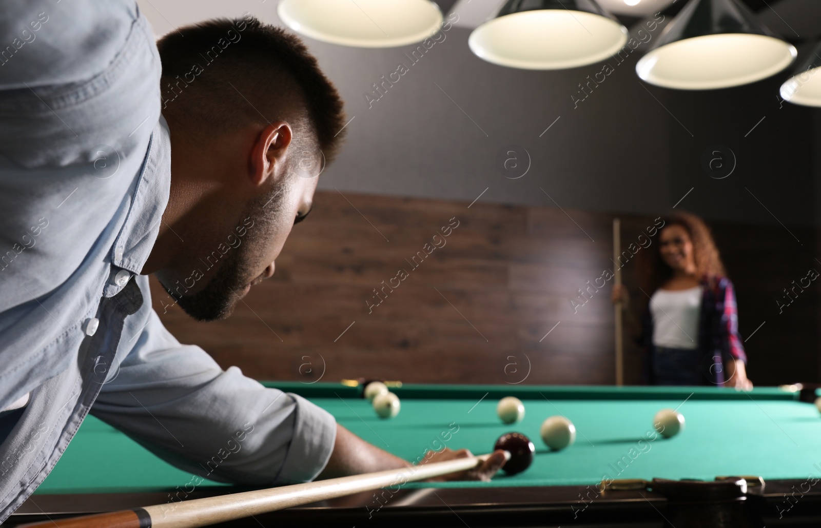 Photo of Young man playing billiard and blurred African-American woman on background. Space for text