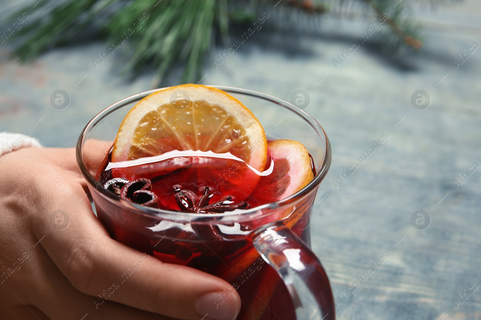 Photo of Woman holding cup with red mulled wine on table, closeup