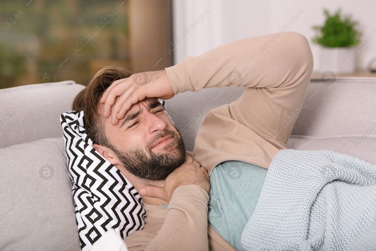 Photo of Ill man suffering from cough on sofa at home