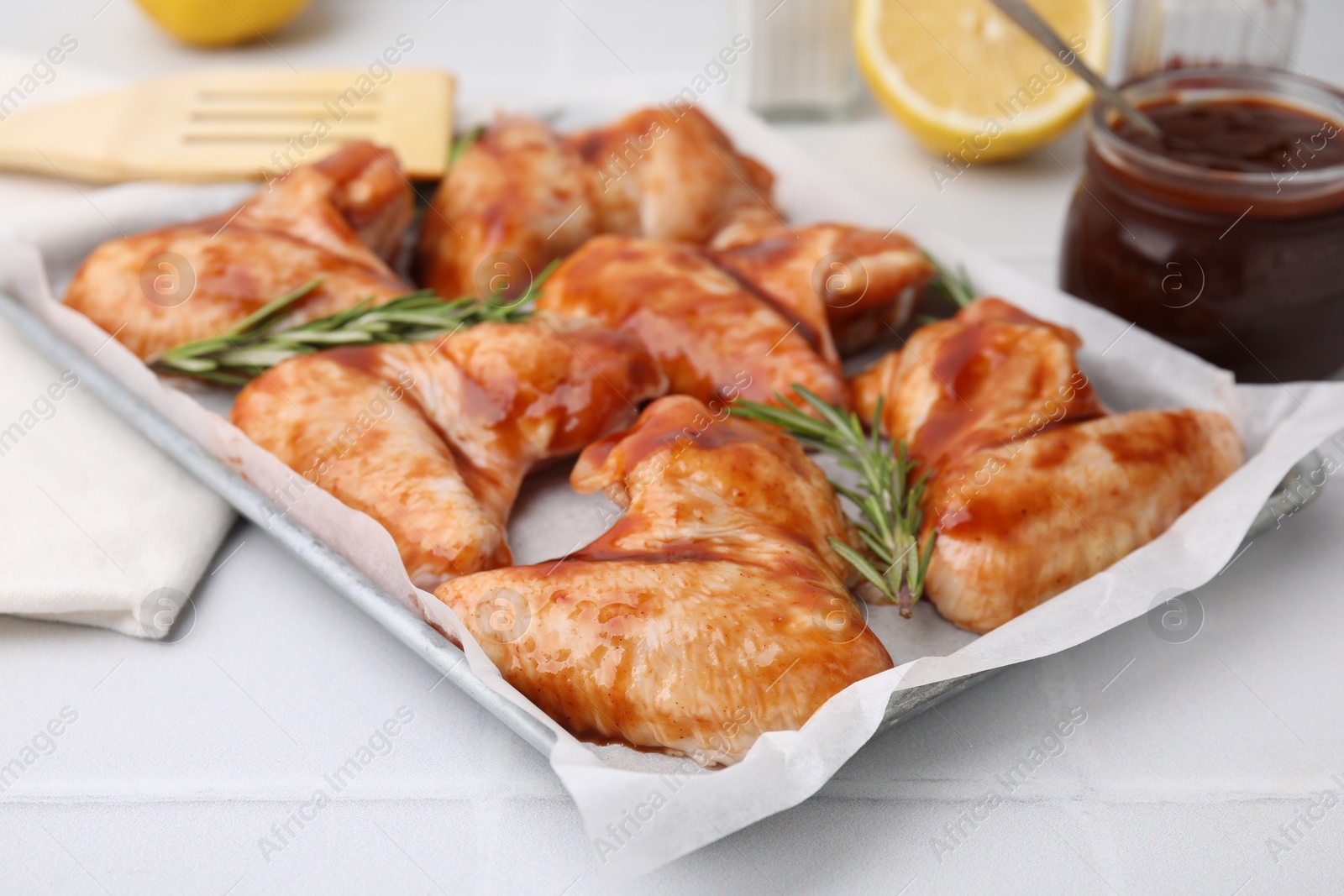 Photo of Raw marinated chicken wings and rosemary on light tiled table, closeup