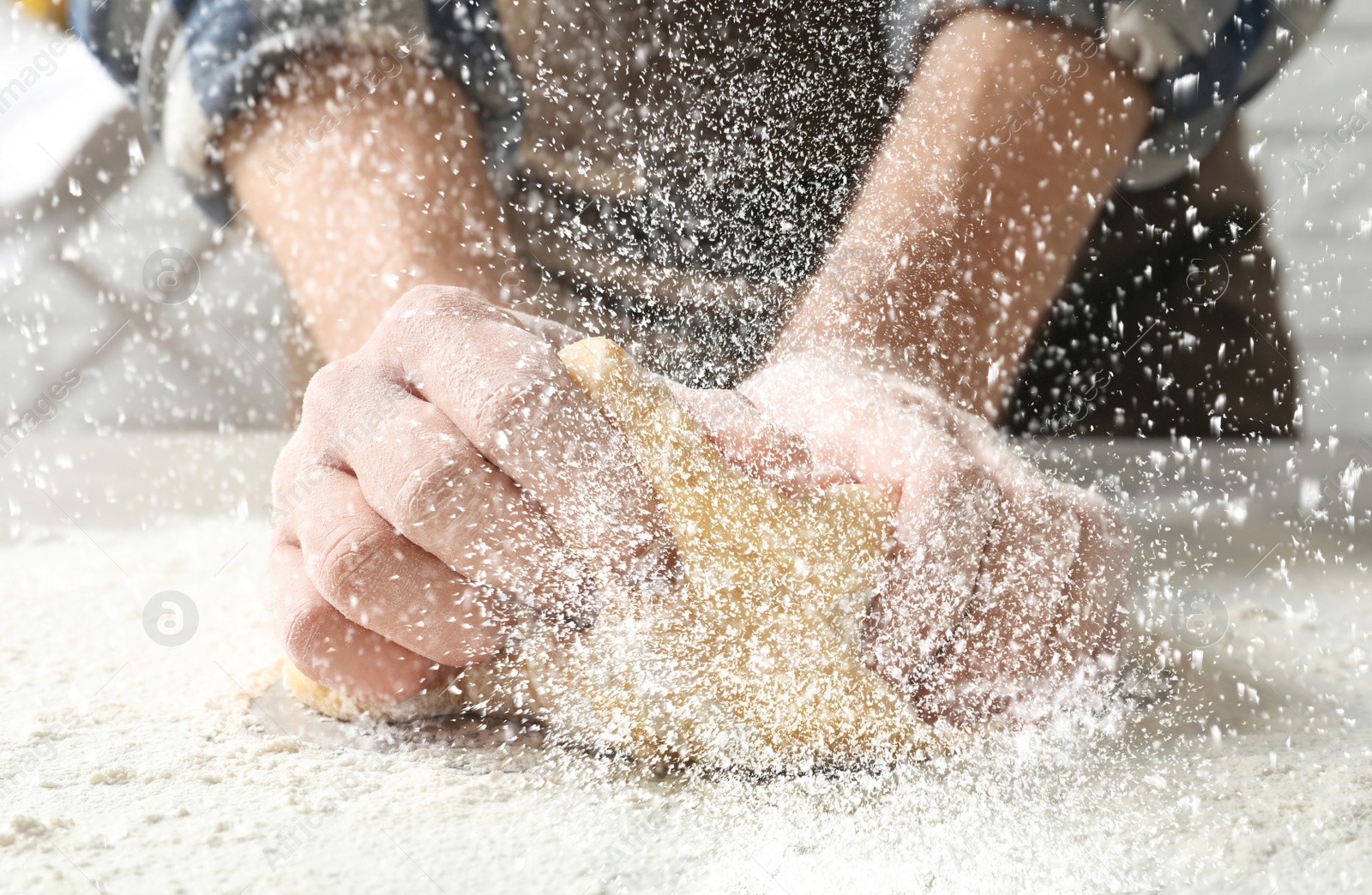 Image of Young man kneading dough at table in kitchen, closeup