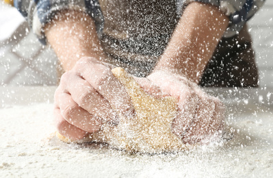 Image of Young man kneading dough at table in kitchen, closeup