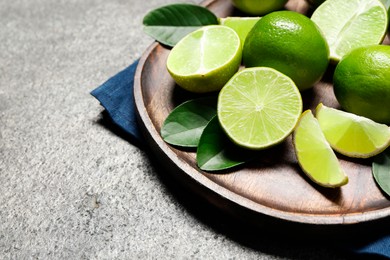 Photo of Fresh ripe limes and leaves on grey table, closeup. Space for text