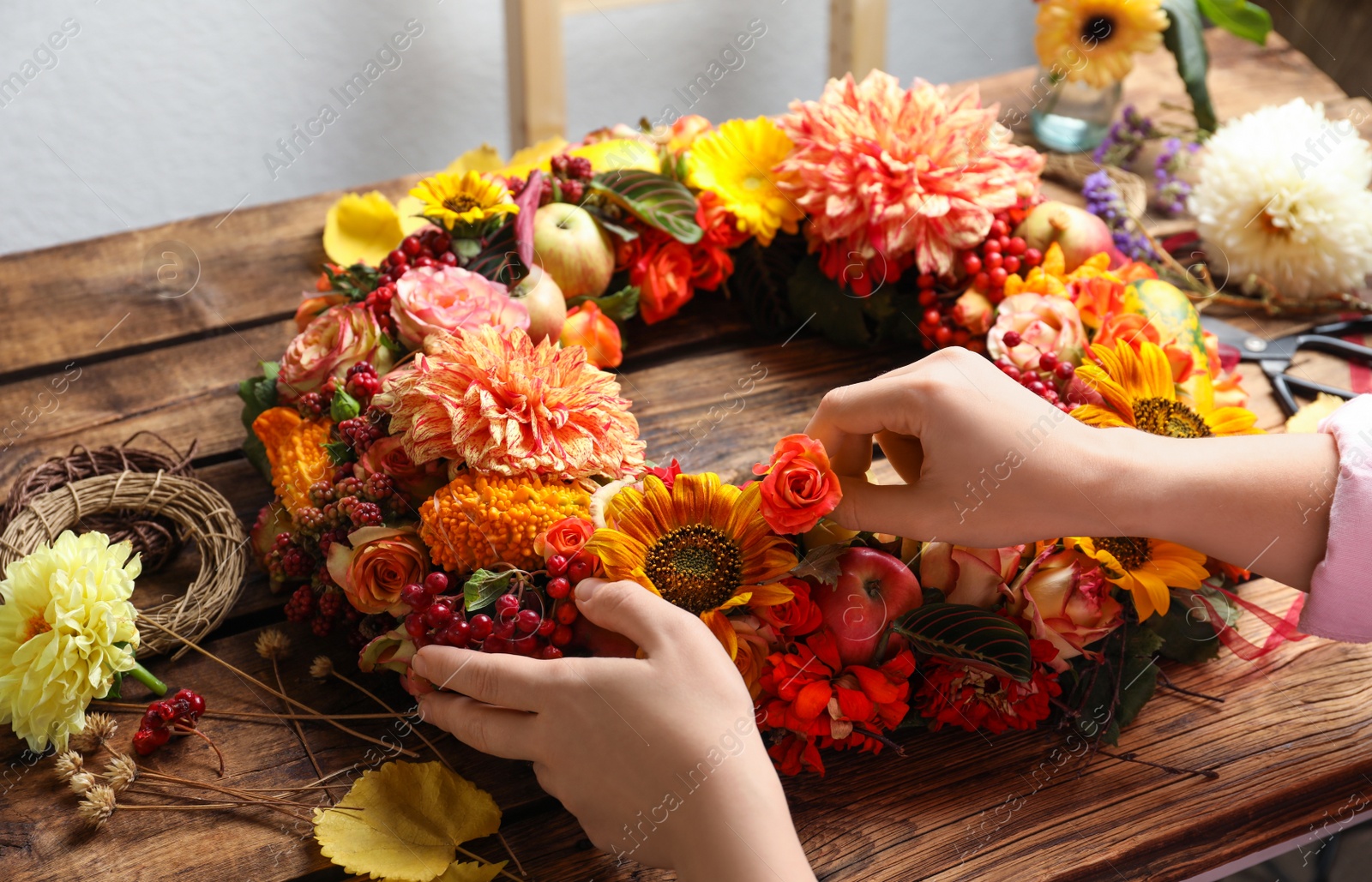 Photo of Florist making beautiful autumnal wreath with flowers and fruits at wooden table, closeup