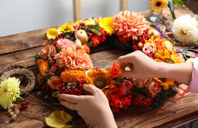 Florist making beautiful autumnal wreath with flowers and fruits at wooden table, closeup