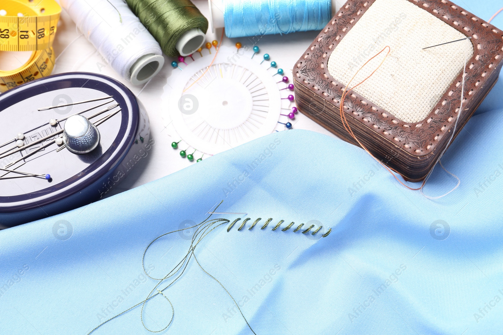 Photo of Light blue cloth with needle, thread and stitches near sewing tools on table, above view