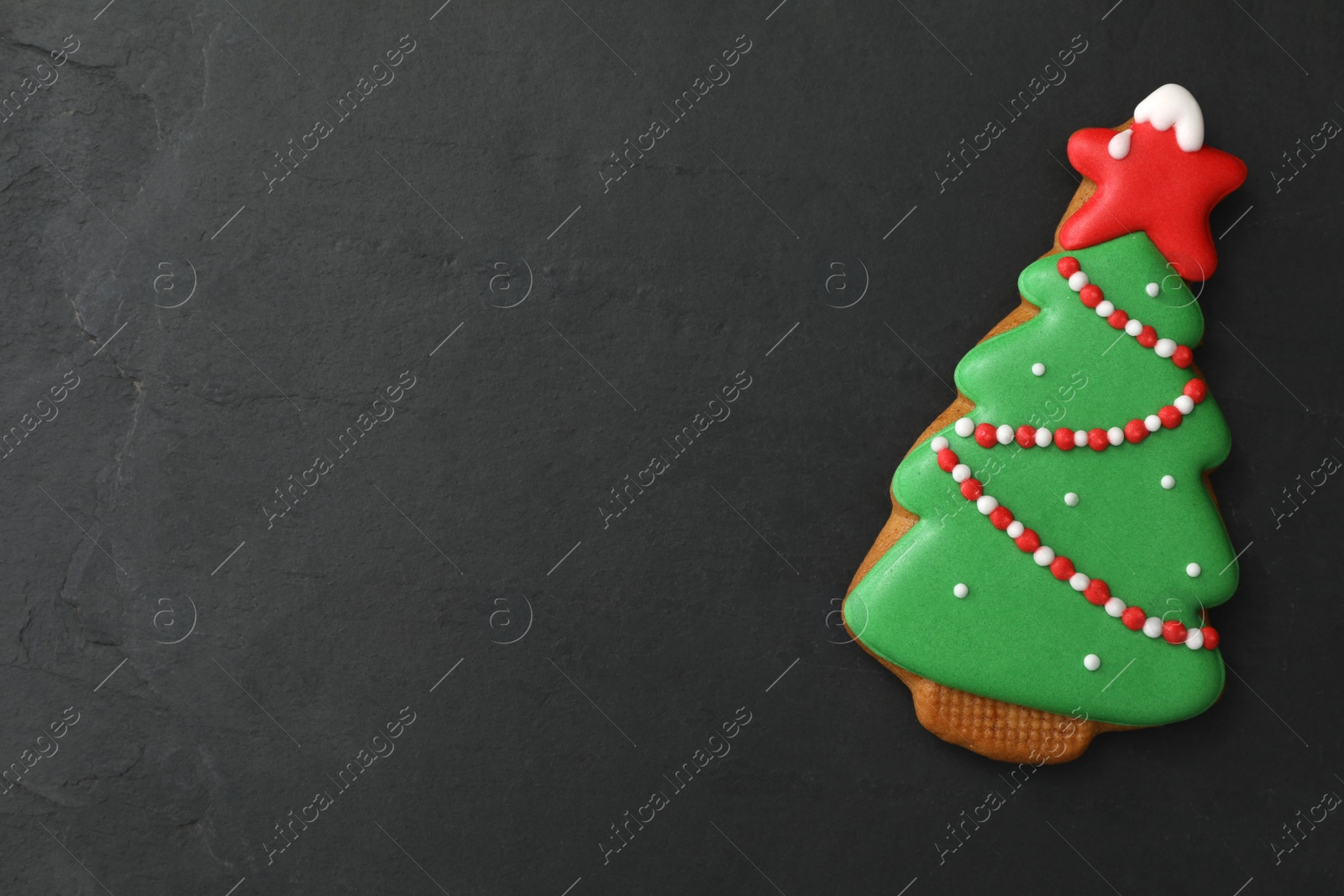 Photo of Christmas tree shaped cookie on black table, top view. Space for text