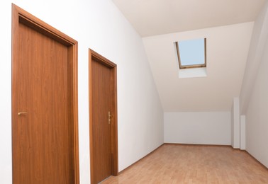 Photo of Light spacious attic room with doors and window on slanted ceiling