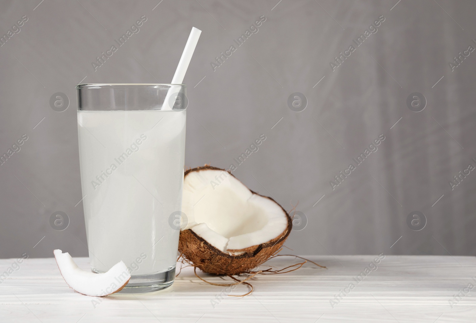 Photo of Glass of coconut water and nut on white wooden table. Space for text