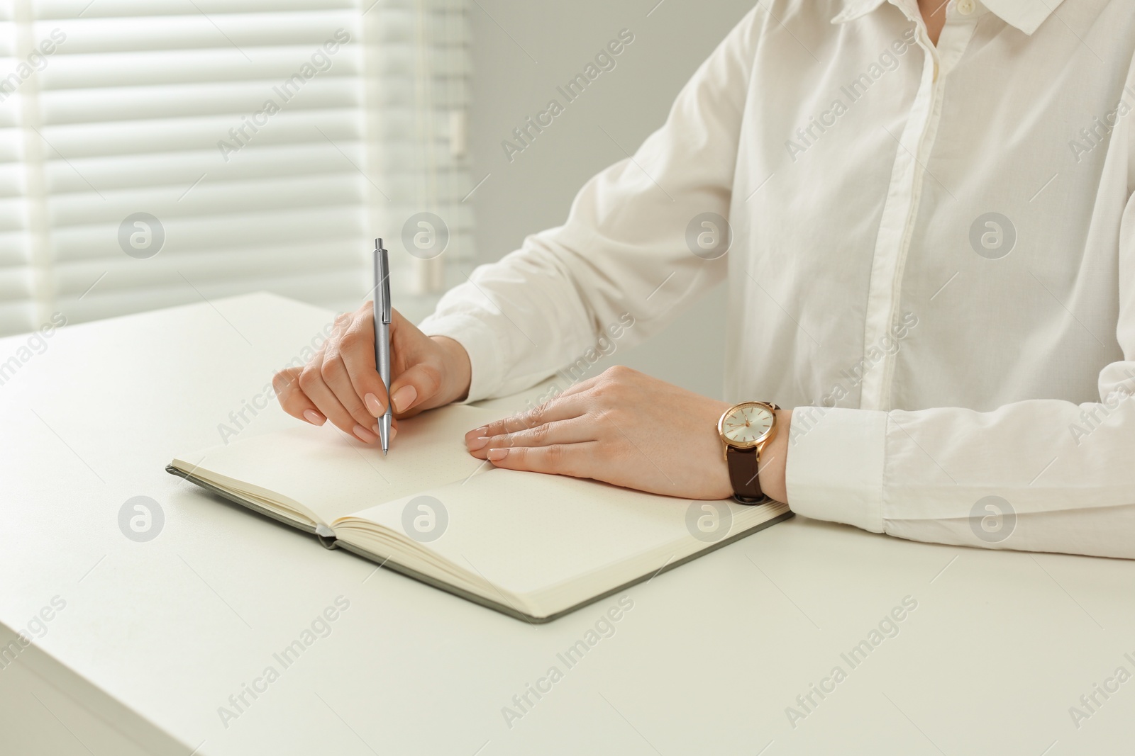 Photo of Woman writing in notebook at white table, closeup