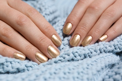 Woman with golden manicure holding knitted fabric, closeup. Nail polish trends