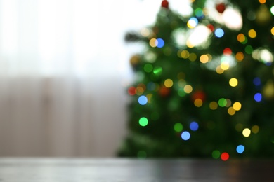 Photo of Blurred view of fir tree with glowing Christmas lights near table indoors