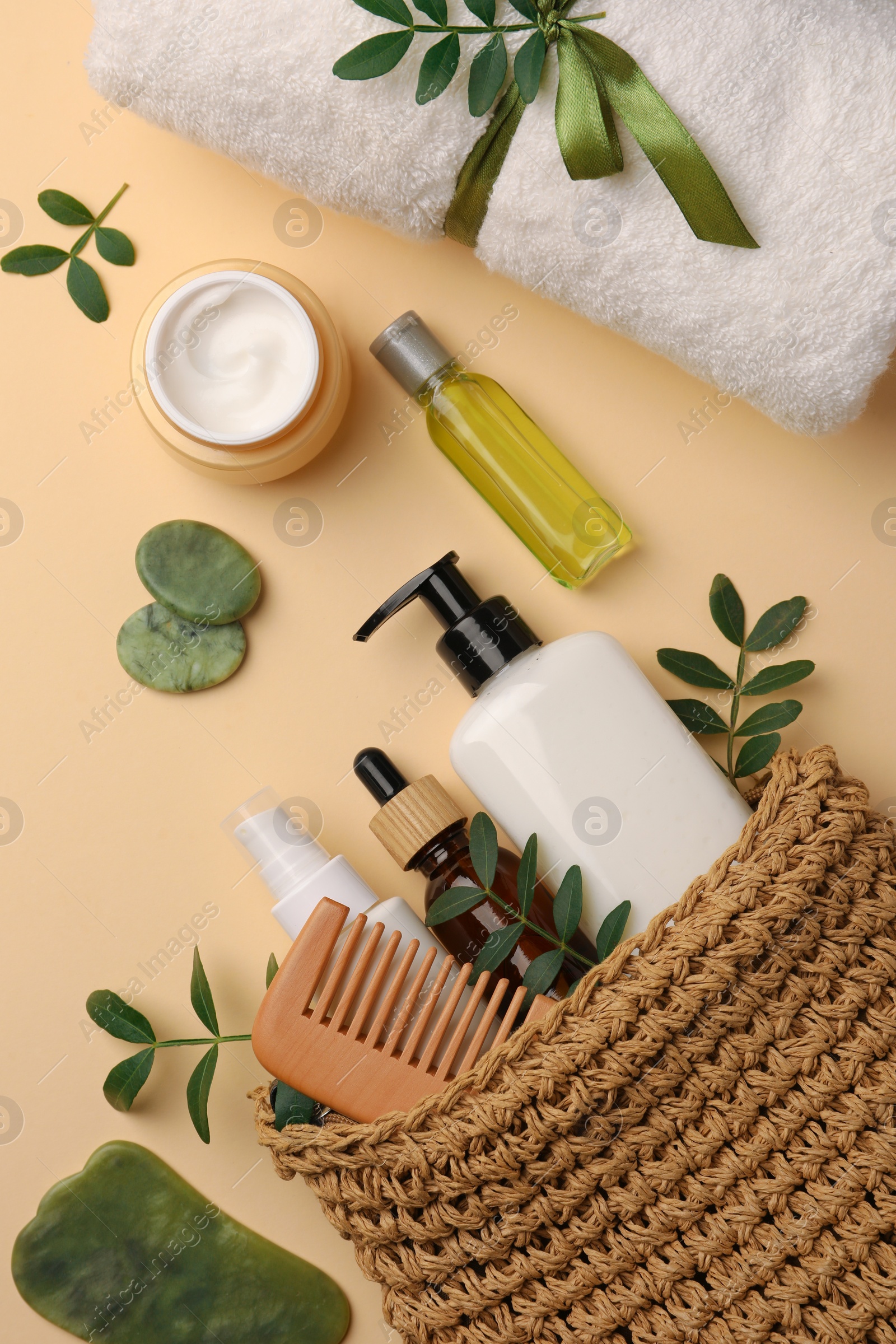 Photo of Compact toiletry bag with different cosmetic products, spa stones and towel on beige background, flat lay