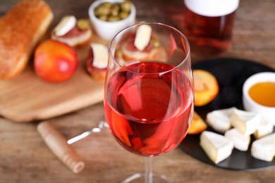 Glass of delicious rose wine and snacks on table, closeup