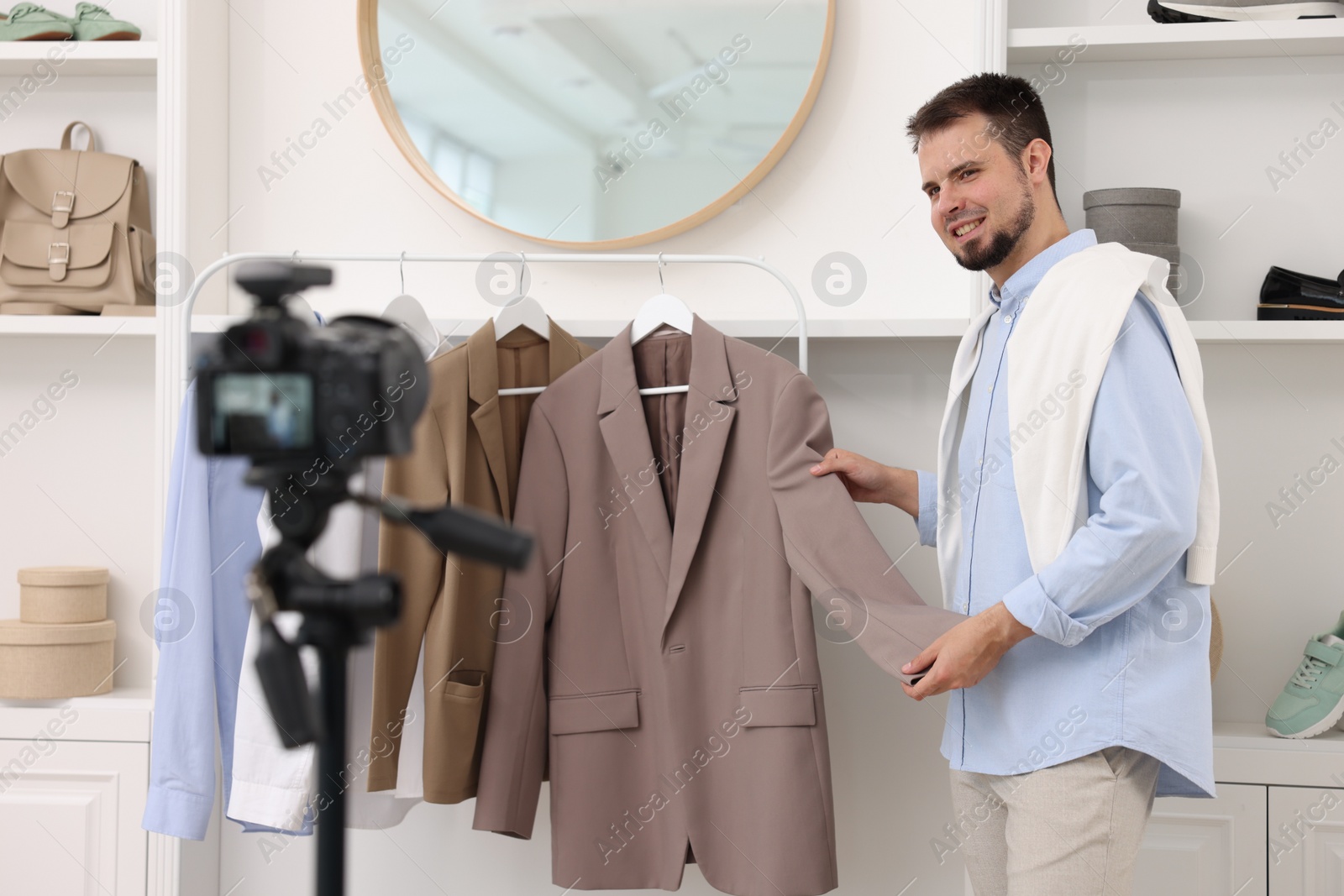 Photo of Smiling fashion blogger showing clothes while recording video at home