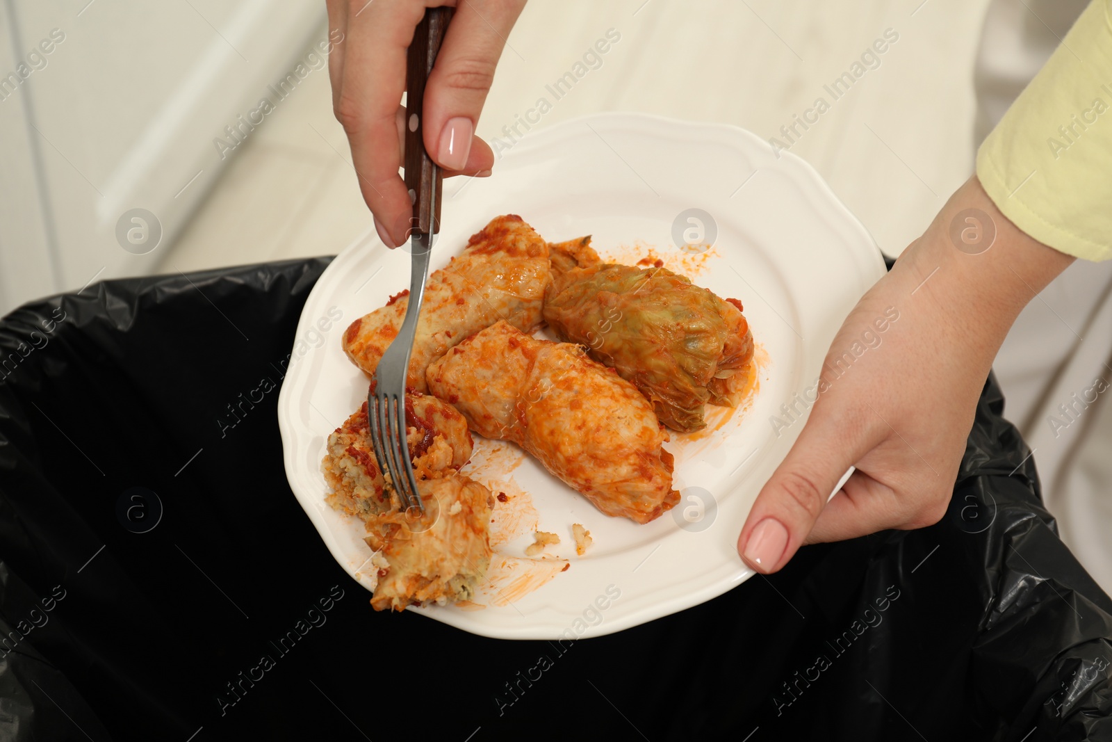 Photo of Woman throwing cabbage rolls into bin indoors, closeup