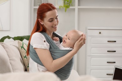 Mother holding her child in sling (baby carrier) at home