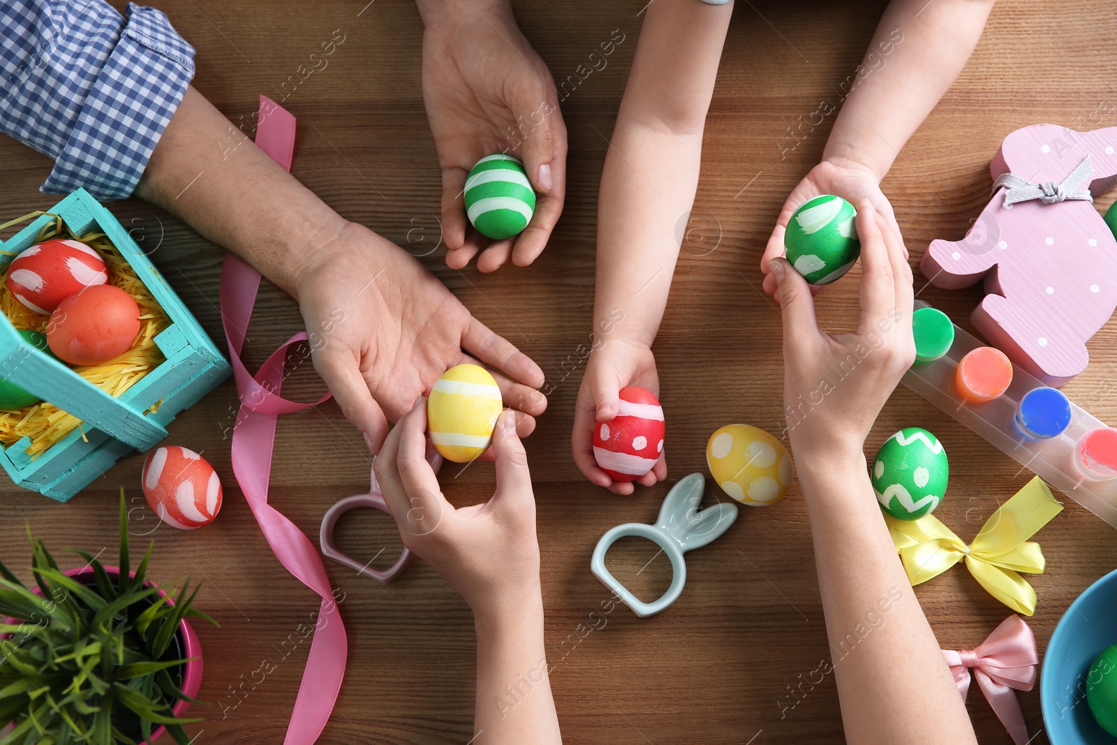 Photo of Father, mother and their child holding painted Easter eggs on wooden background, top view