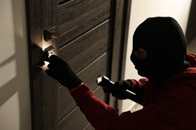 Photo of Thief with flashlight breaking foreign door's lock in hall. Burglary