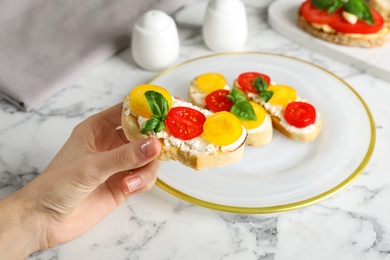 Photo of Woman eating tasty fresh tomato bruschettas at marble table, closeup