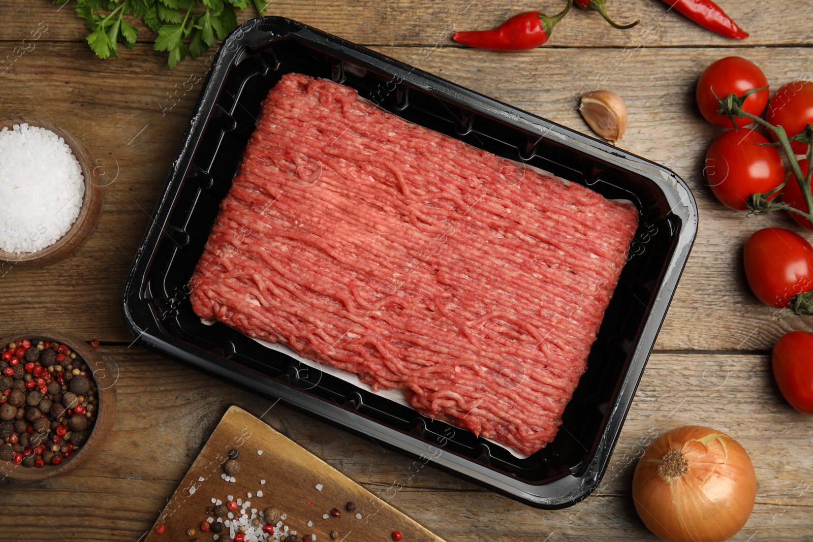 Photo of Raw fresh minced meat, tomatoes and other ingredients on wooden table, flat lay