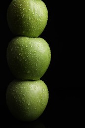 Stack of green apples with water drops on black background