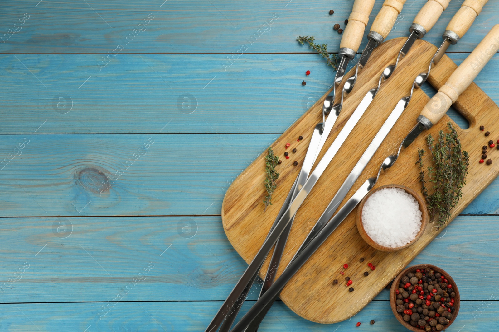 Photo of Flat lay composition with metal skewers on light blue wooden table. Space for text