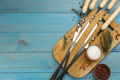 Flat lay composition with metal skewers on light blue wooden table. Space for text