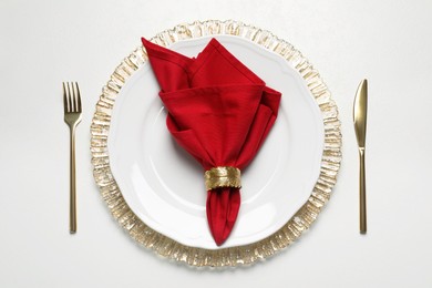 Plate with red fabric napkin, decorative ring and cutlery on white table, flat lay