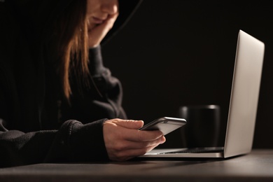 Woman using smartphone at table with laptop in darkness, closeup. Loneliness concept