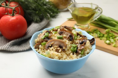 Delicious bulgur with mushrooms, green onion and other products on white table, closeup