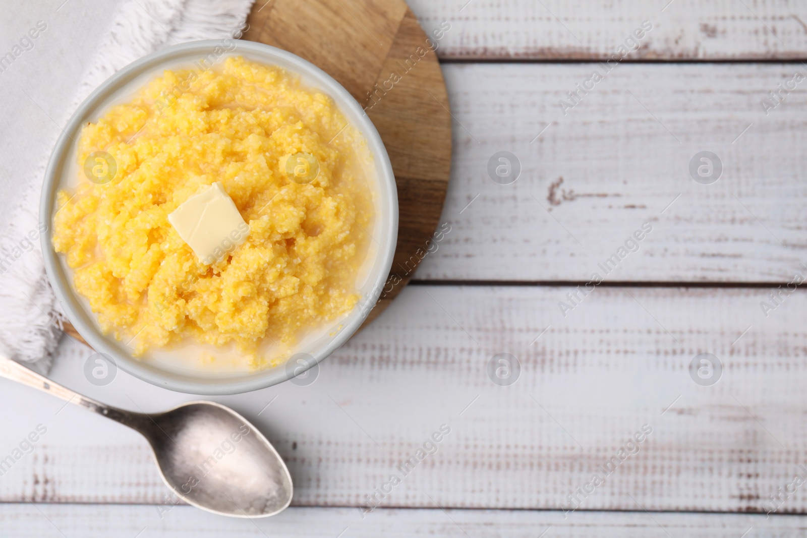 Photo of Tasty cornmeal with butter in bowl served on white wooden table, flat lay. Space for text