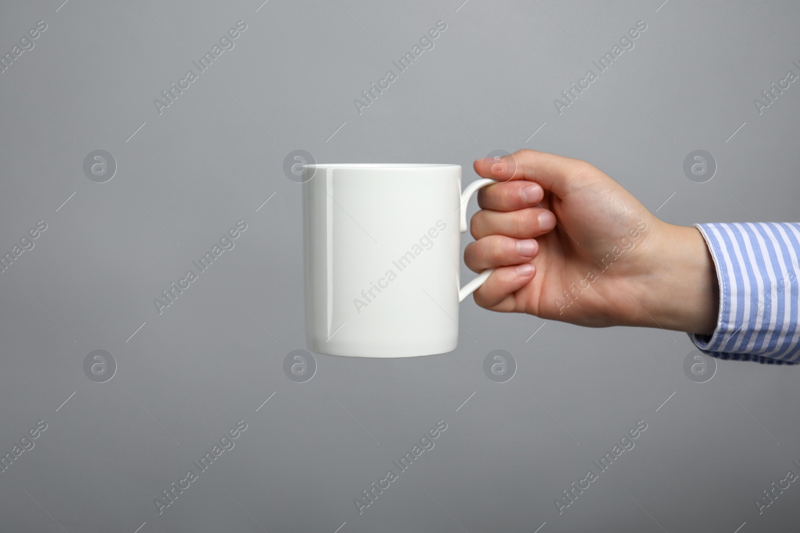 Photo of Woman holding white mug on light grey background, closeup. Space for text