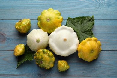 Photo of Fresh ripe pattypan squashes with leaves on light blue wooden table, flat lay