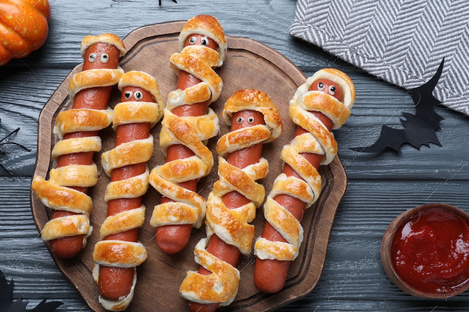 Photo of Cute sausage mummies served on wooden table, flat lay. Halloween party food