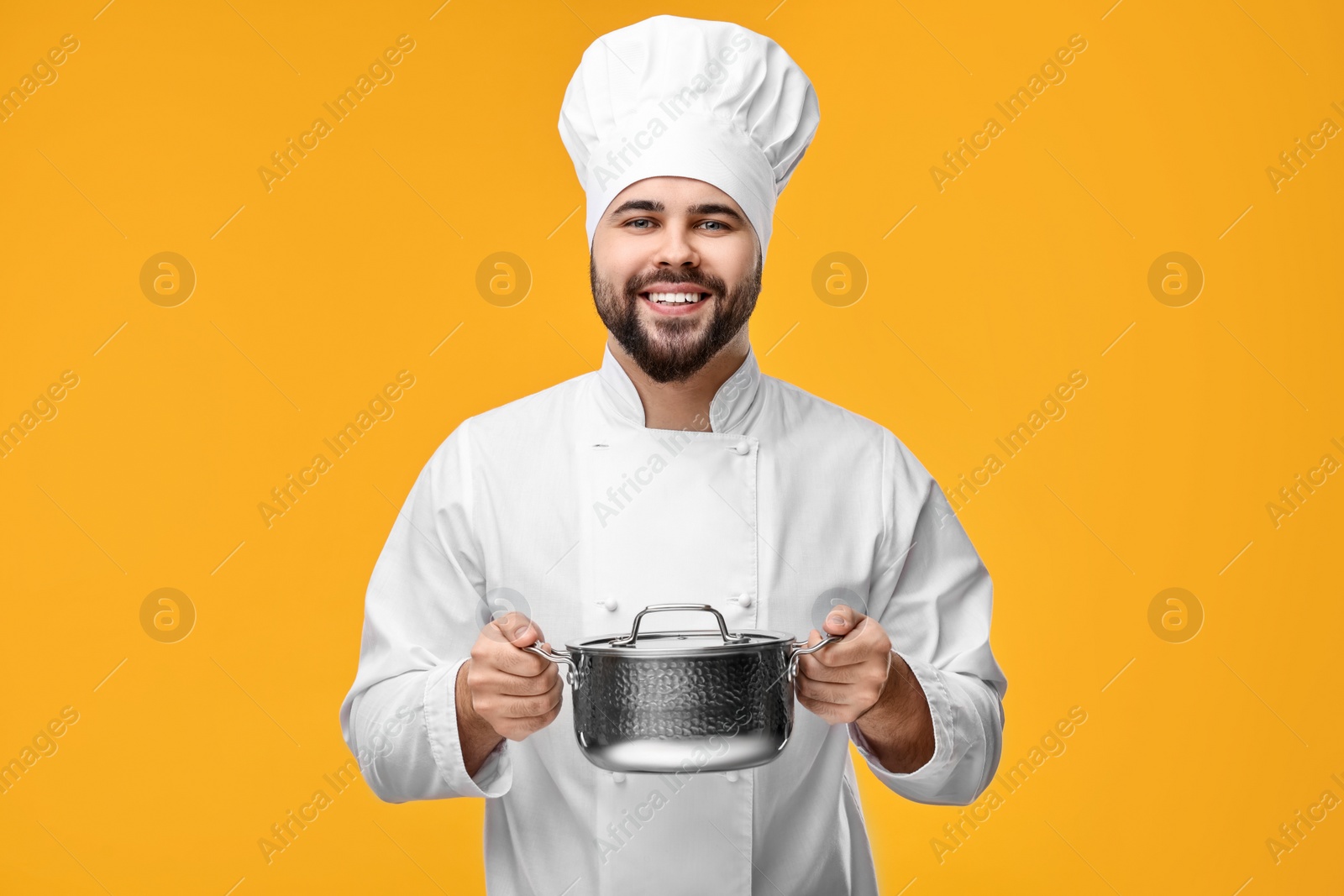 Photo of Happy young chef in uniform holding cooking pot on orange background