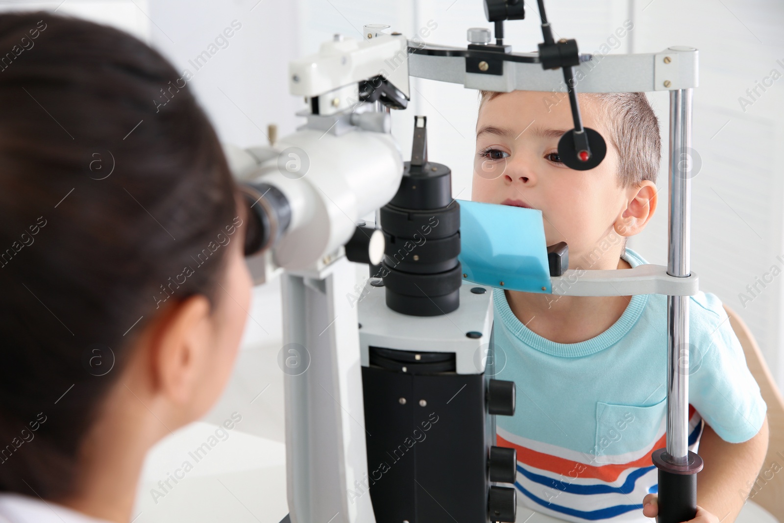 Photo of Children's doctor examining little boy with ophthalmic equipment in clinic