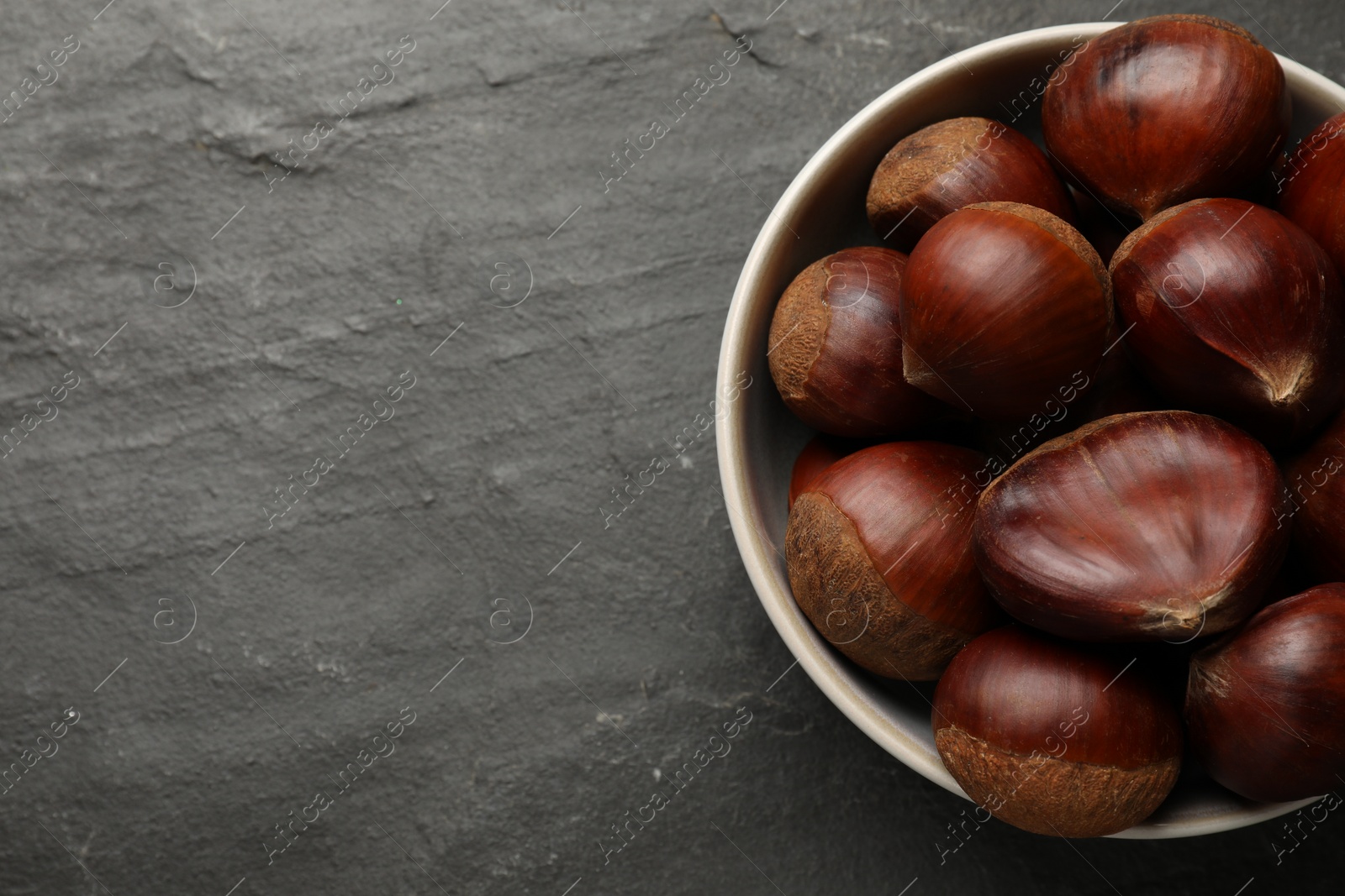 Photo of Roasted edible sweet chestnuts in bowl on grey textured table, top view. Space for text