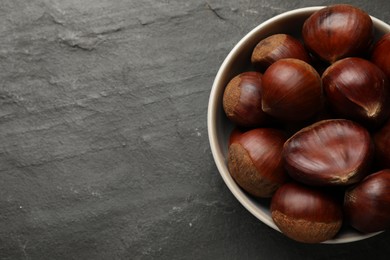 Roasted edible sweet chestnuts in bowl on grey textured table, top view. Space for text