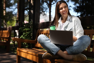 Beautiful woman with coffee working on laptop in park