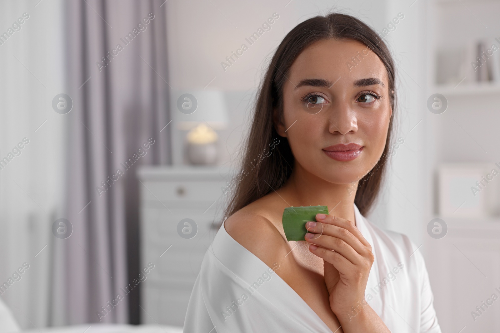 Photo of Young woman applying aloe gel from leaf onto her shoulder indoors. Space for text