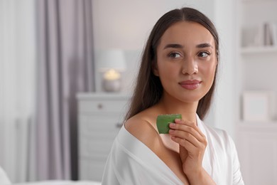 Young woman applying aloe gel from leaf onto her shoulder indoors. Space for text