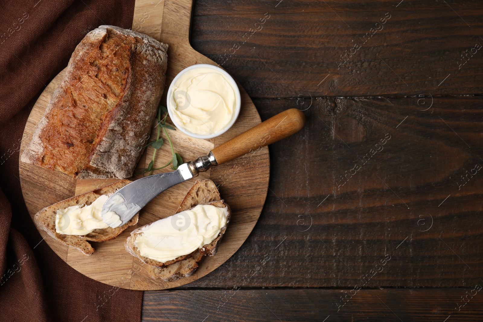 Photo of Tasty bread with butter and knife on wooden table, top view. Space for text