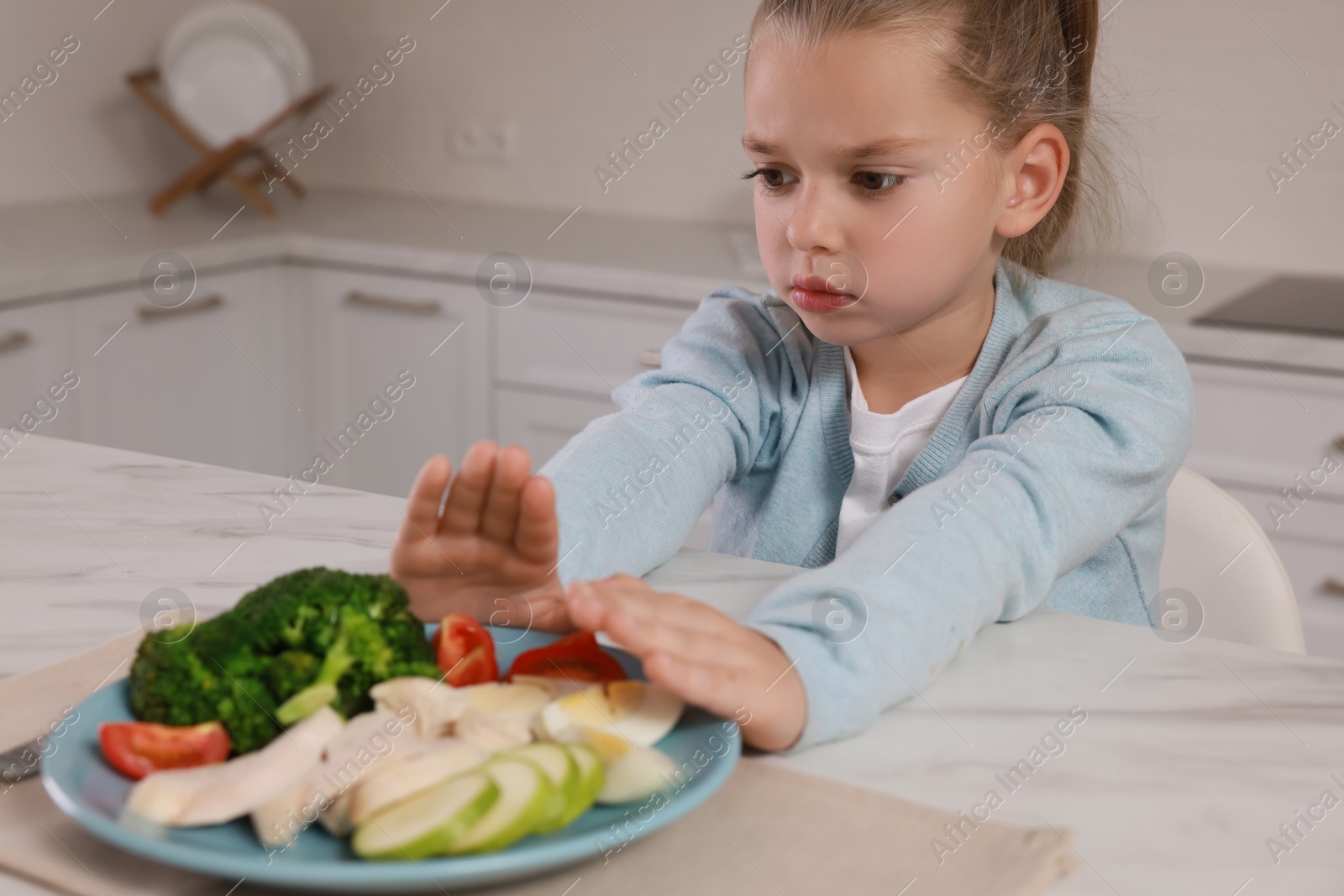 Photo of Cute little girl refusing to eat dinner in kitchen