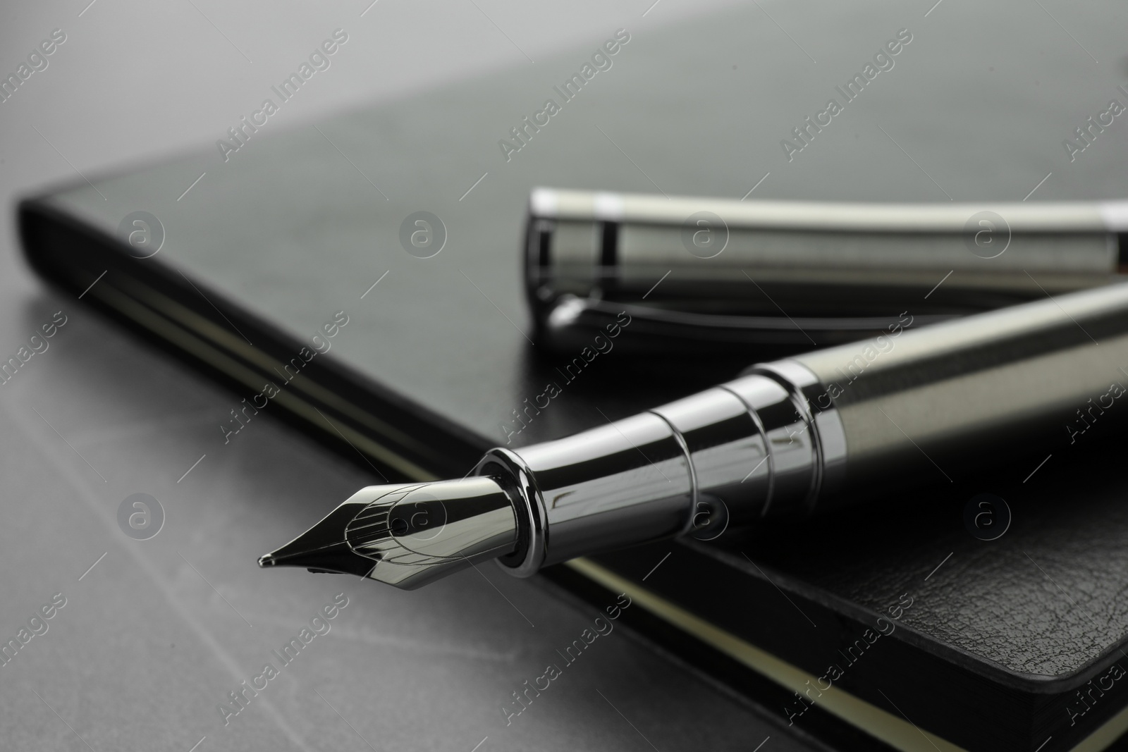 Photo of Stylish fountain pen, cap and leather notebook on light grey textured table, closeup