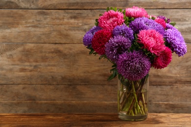 Photo of Beautiful asters in vase on table against wooden background, space for text. Autumn flowers